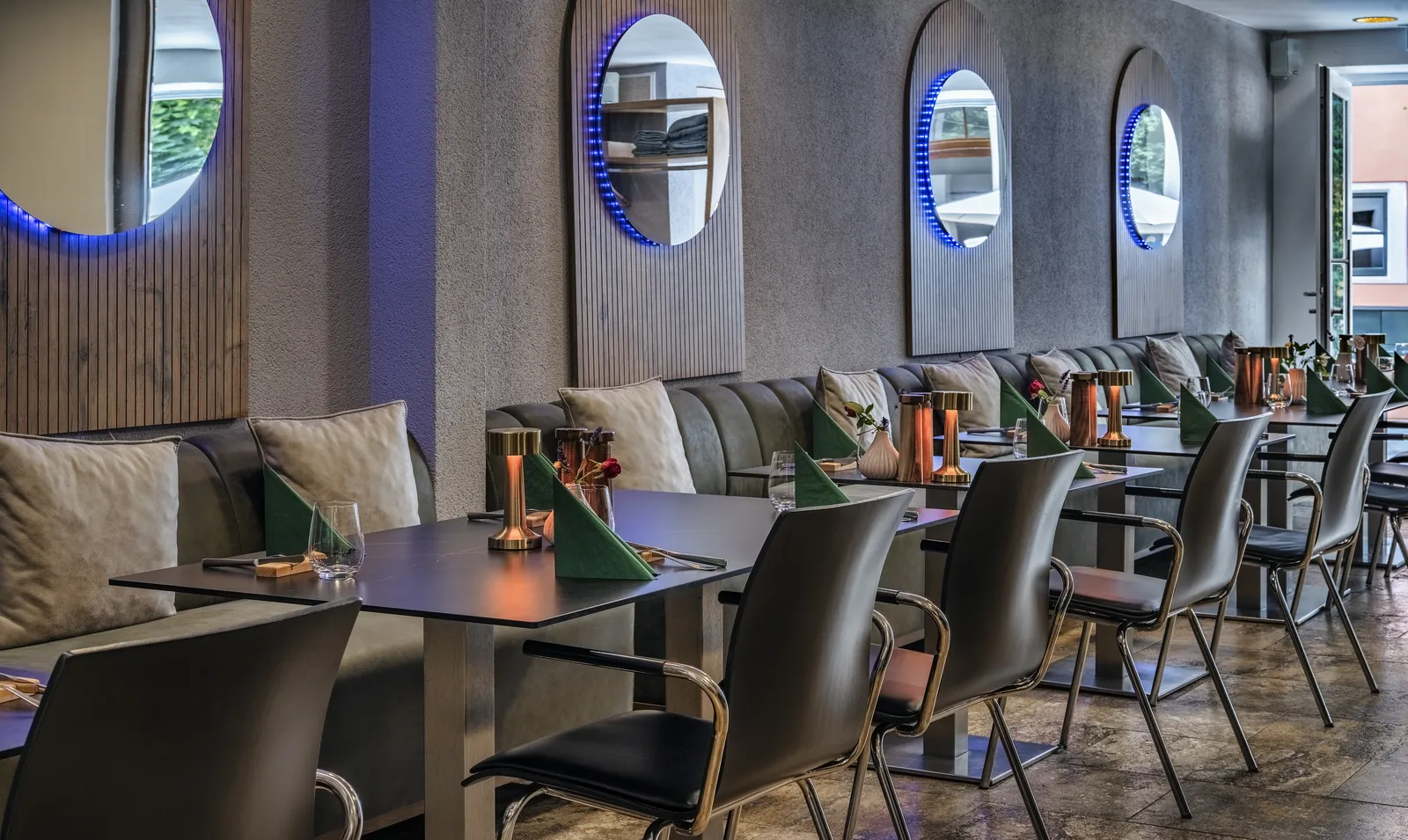 The Amaris dining room with its banquette, dark tables, green napkins and four illuminated round mirrors on the wall
