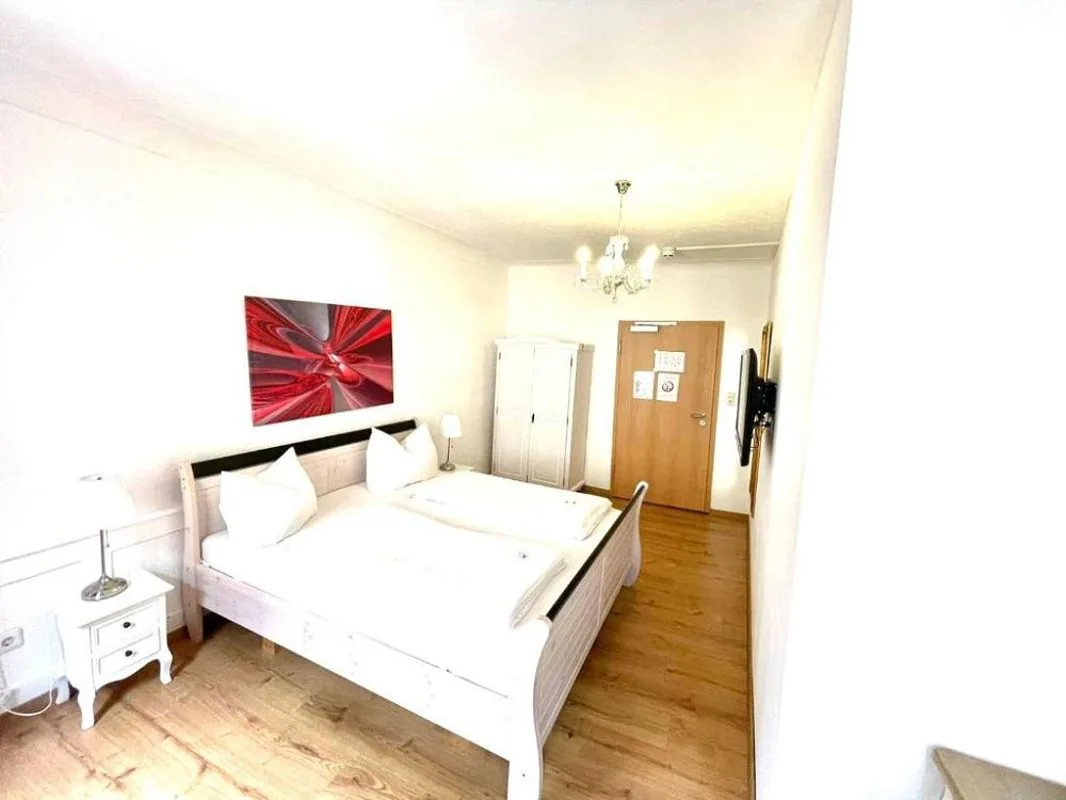 Chambre double avec salle de bain à l’étage : lit double blanc, tableau rouge, lustre et parquet